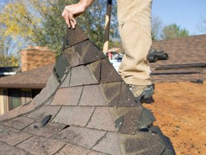 A worker removing old shingles during the roof restoration process, revealing the wooden roof structure underneath.