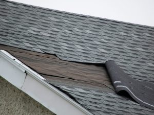 A close-up of weathered, worn-out roof shingles, showing signs of significant damage and deterioration.