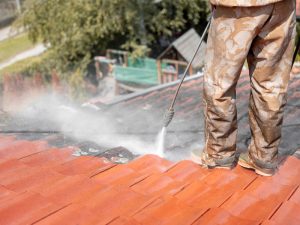 A worker pressure washing a residential roof, restoring its shine and removing dirt and grime. Roof Pressure Washing