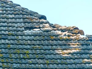 A weathered roof with missing tiles and moss growing on the tiles. Consider removing roof algae to protect your roof.